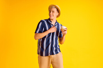 Handsome smiling young man in striped shirt, shorts and straw hat eating delicious vanilla ice...