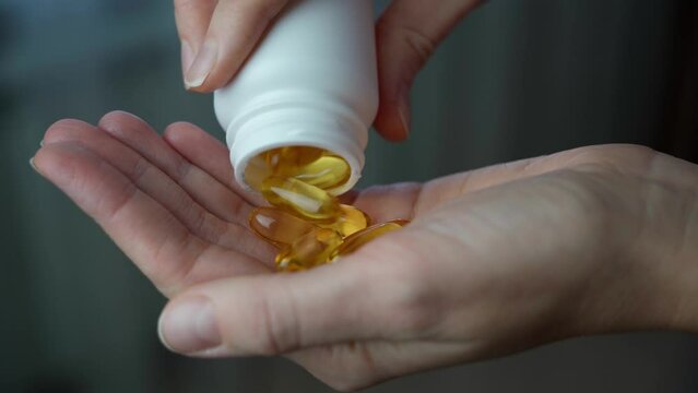 Close-up of a woman pouring vitamin D or omega-3 into her hand. Healthcare and medicine, well-being and immunity.
