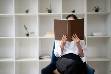 A picture of a woman sitting and reading with a book covering her face. - obrazy, fototapety, plakaty