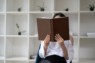 A picture of a woman sitting and reading with a book covering her face. - obrazy, fototapety, plakaty