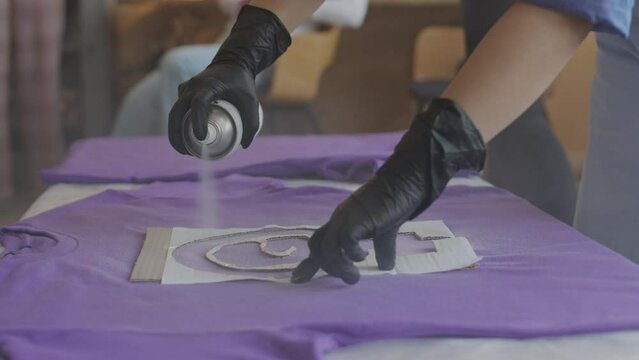 Cropped shot o unrecognizable woman in black gloves painting feminist symbol in purple cotton t-shirt using fabric spray paint and stencil while making uniform before going on demonstration protest