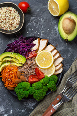 The concept of proper, nutritious nutrition, a bowl with chicken breast, buckwheat, vegetables, cabbage, broccoli, carrots, nuts, avacado and cherry tomatoes on a dark background, top view.