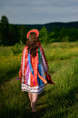 The girl, with her back turned and dressed in Ukrainian national clothes, walks barefoot in the field.