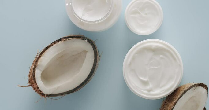 White Bottles and tubes with coconut for cosmetics rotating on a light blue background in studio. Natural cosmetics production for hair and skin care. Glossy cosmetic jar with cream. Top view.