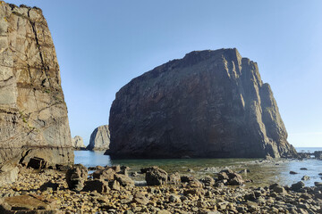 a rocky coastline with large cliffs under a clear blue sky and calm deep blue water