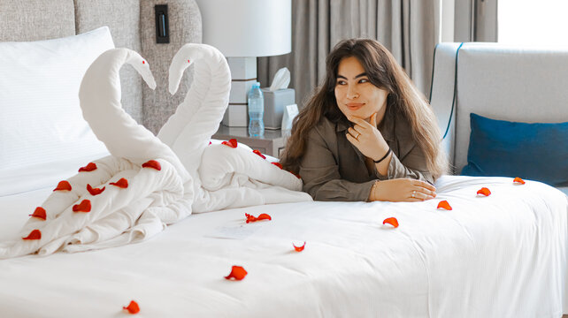 Portrait of the woman with Swan towel decoration on bed with white pillow in bedroom interior. High quality photo