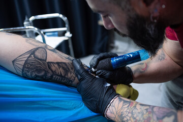 A male tattooist drawing a tattoo on a male leg skin in a tattoo studio closeup