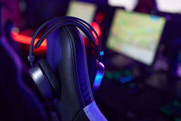 Close up of wireless headset on gaming chair in cybersports club lit by neon lights, copy space