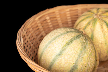 Two sweet melons in a straw bowl, macro, isolated on a black background.