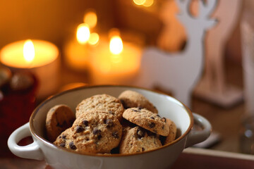 Bowl of cookies, cup of tea, dry oranges, pine cones, books, reading glasses, small presents, various Christmas decorations and lit candles on the table. Cozy Christmas hygge. Selective focus.