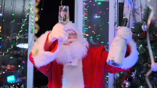 Cheerful Santa Claus with champagne flute in hand and bottle sways to beat of music, says toast, sings to have fun at Christmas party decorated with colorful garlands and tinsel hanging from ceilings.