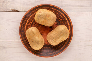 Three ripe kiwis in a clay plate on a wooden table, macro, top view.