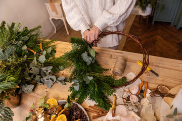 Top view composition of female hands making Christmas wreath from natural branches of spruce, pine