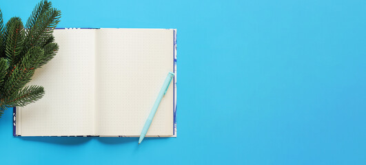 Open notebook with pen on a blue background, spruce branch, top view, empty space. Copy space. Christmas branch and diary for notes
