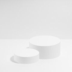 Abstract white stage with two white round podiums mockup for cosmetic products in hard light on white background. Scene for presentation cosmetic products, gifts, goods, advertising, design, sale.