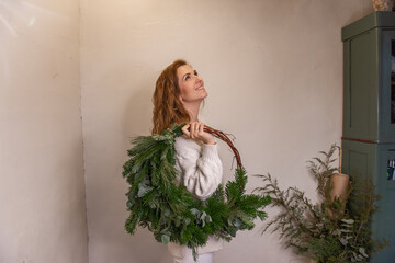Portrait of young woman holding asymmetrical green Christmas wreath made of natural materials
