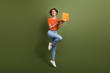 Full size photo of impressed excited woman dressed orange shirt hold laptop jumping find sale in eshop isolated on khaki color background