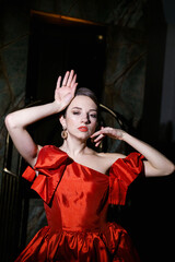 Fototapeta premium Pretty woman in a luxurious red dress posing in a luggage trolley.Fashion shooting concept
