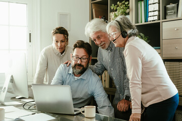 Obraz premium Group of old and middle age business people in office working and using laptop while sitting at the office desk together discussing project details and opinions