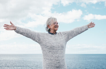 Smiling caucasian elderly woman with open arms in travel, retirement o vacation at sea enjoying...
