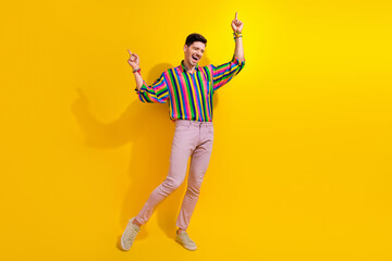 Fototapeta na wymiar Full length photo of young guy in stylish garment point fingers up enjoying rhythm soundtrack at party isolated on yellow color background