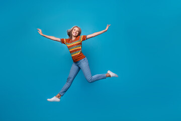 Fototapeta na wymiar Full length photo of positive excited girl dressed print shirt jumping high arms sides empty space isolated blue color background
