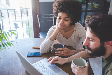 Young multiethnic couple using pc having coffee running small business