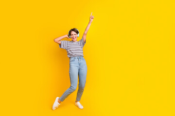 Fototapeta na wymiar Full length portrait of crazy person touch headphones point finger rejoice empty space isolated on yellow color background