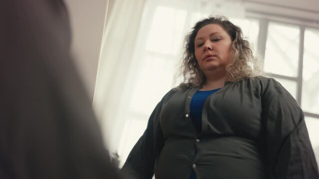 Fat woman buttoning tight shirt, upset with mirror reflection, health problem
