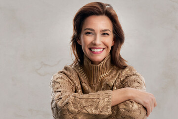 Studio portrait of a brunette haired woman wearing gold sweater and cheerful smiling against isolated background