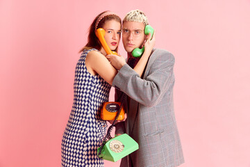 Young man and woman, employees, co-workers talking on retro phones against pink studio background. Concept of emotions, business, profession and occupation, lifestyle, teamwork, cooperation