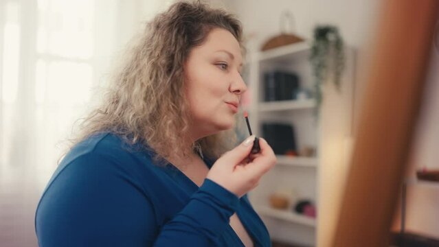 Happy plus size woman applying lipstick and smiling, doing makeup for date