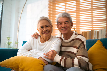 Sweet older couple enjoys quiet time together, seated comfortably on their vintage couch in a warm,...