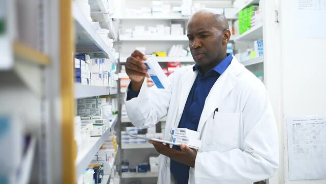 Black man, pharmacist and tablet with box on shelf for medication, inventory inspection or dispensary. African male person or doctor with technology checking pharmaceutical stock or drugs at pharmacy