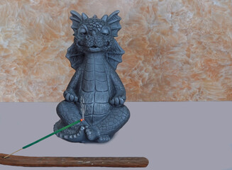 A figurine of a gray meditating dragon with a lit incense stick, for a poster, postcard.