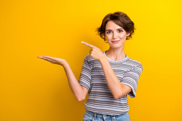 Portrait of positive girl with short hairstyle wear grey t-shirt indicating at empty space on palm...