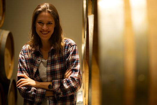 Portrait of a young woman surrounded by wine barrels In her winery