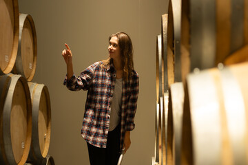 Portrait of a young woman surrounded by wine barrels In her winery