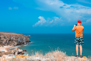 man stands on the top of a mountain and films the sea and mountains with his camera. Travel and...