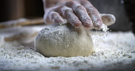 Super slow motion of professional artisan baker chef kneads dough with flour while making homemade bread, pasta or pizza on rustic wooden table in traditional bakery kitchen.
