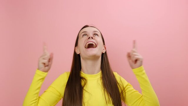 Portrait of pleasantly surprised pretty young caucasian woman pointing up and looking with shocked face, showing copy space for commercial, posing isolated over pink color background wall in studio
