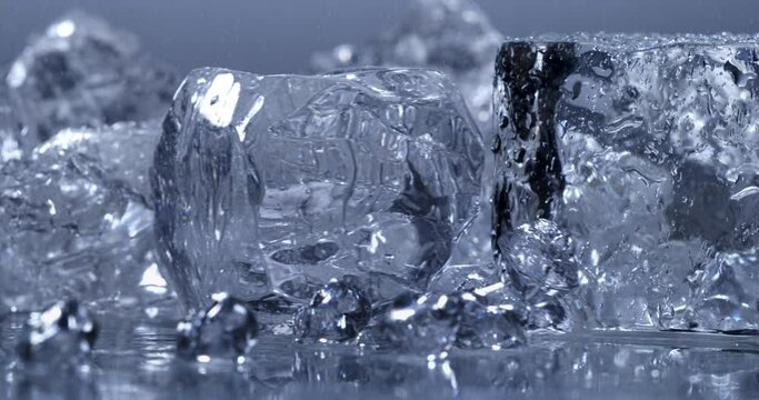 Super slow motion top view close up of ice cool cubes are falling with splashing water drops in transparent clear glass with pure fresh crystal liquid isolated on  frozen background