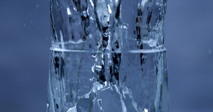Super Slow Motion Detail Shot of Ice Cubes crystals of pure water  Falling into Glass With Alcohol Liquid at 1000 fps in blue environment.