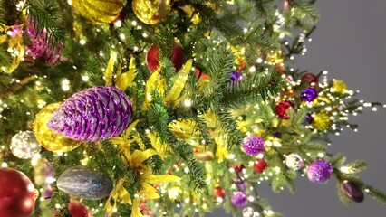 Low angle close-up view of glass purple cone shaped bauble hanging on Christmas tree on night city square. Slow motion vertical video. Soft focus. Winter holidays theme. - Powered by Adobe
