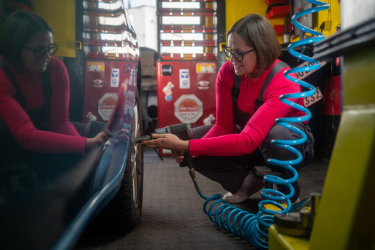 Professional female mechanic doing a wheel replacement in the auto repair shop. Mechanic adjusting the tire at repair garage alone, in grey uniform, woman working in auto repair shop