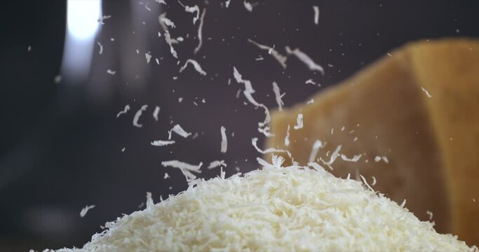 Super slow motion macro of a professional chef grating traditional parmesan cheese with steel grater on the dish close up and pieces of cheese fall at 1000 fps for preparing pasta.