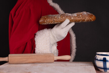 Santa Claus in traditional costume with a whole wheat loaf on a black background.