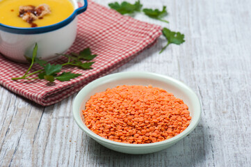 High angle view of red lentils in a bowl on a white vintage wooden table with a bowl of classical Turkish red lentil soup and a few twigs of fresh parsley in the background
