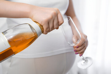 Pregnant woman pours an alcoholic drink into a glass. Negative effects of alcohol on the fetus