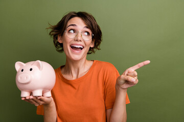Photo of girl wearing specs hold pig wallet collecting coins direct finger empty space to spend...